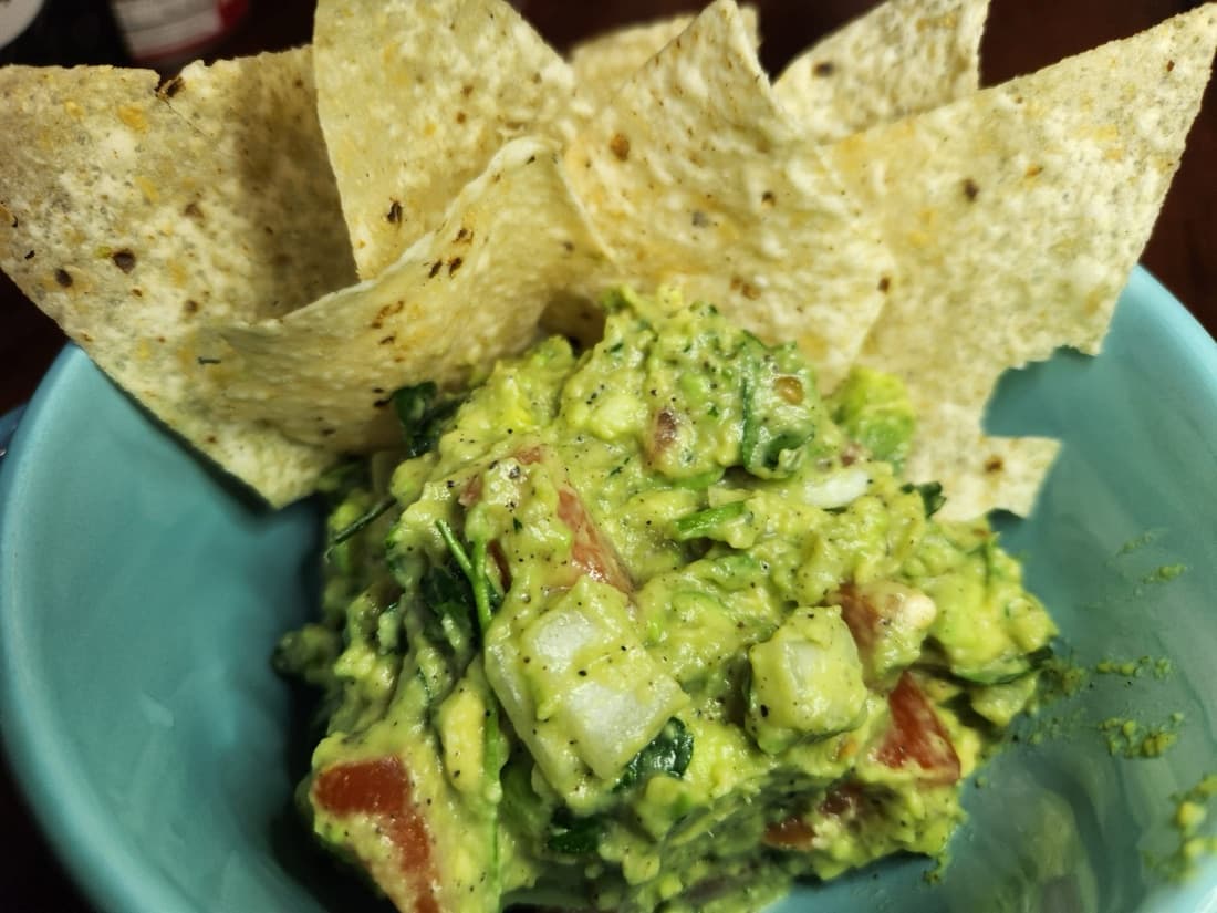 Chicharrones and tortilla chips scooped through a bowl of guacamole